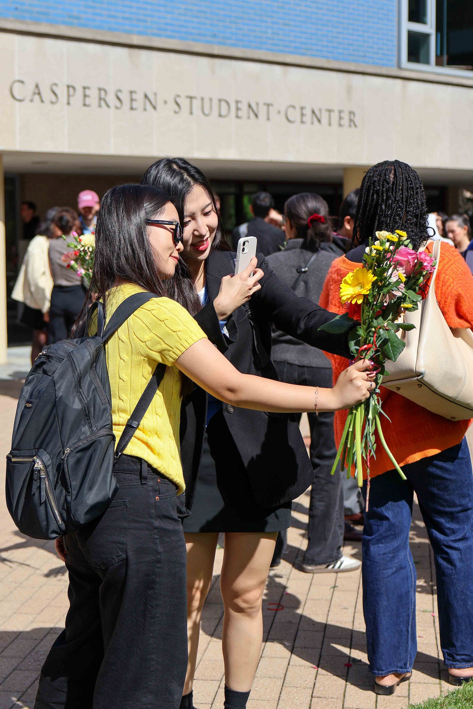 Students in a courtyard take pictures of a bouquet of flowers.
