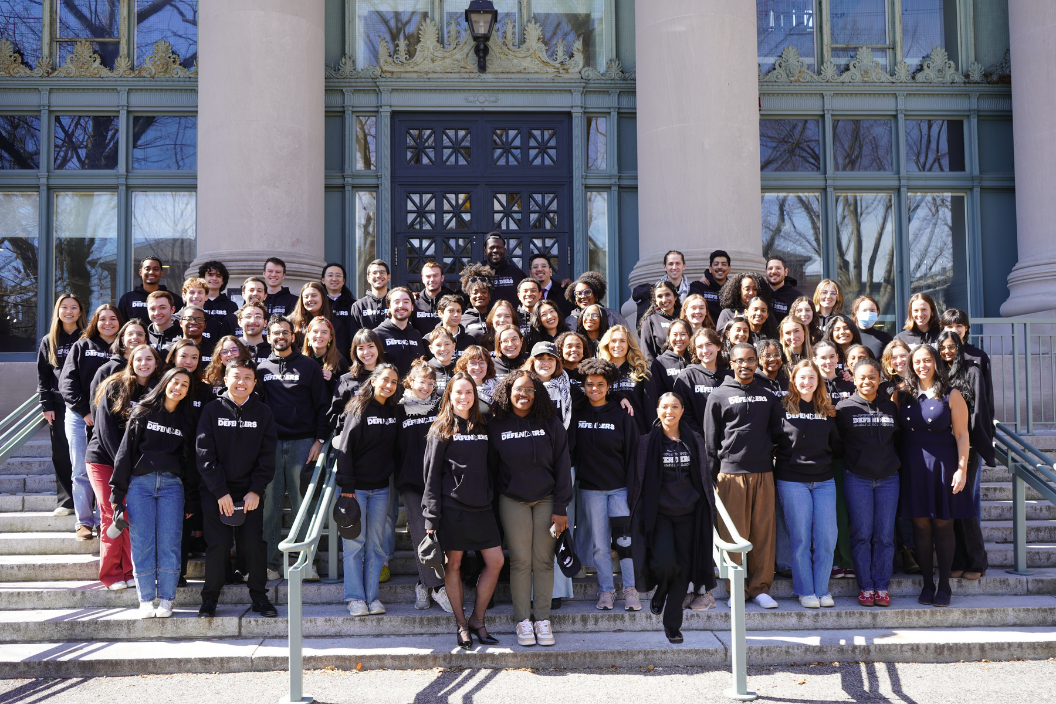 About 100 Harvard Defenders members stand on the steps of Langdell Hall