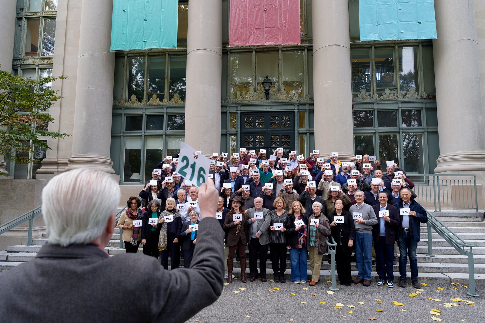 A group of alumni pose for pictures holding cards on the steps of Langdell Hall