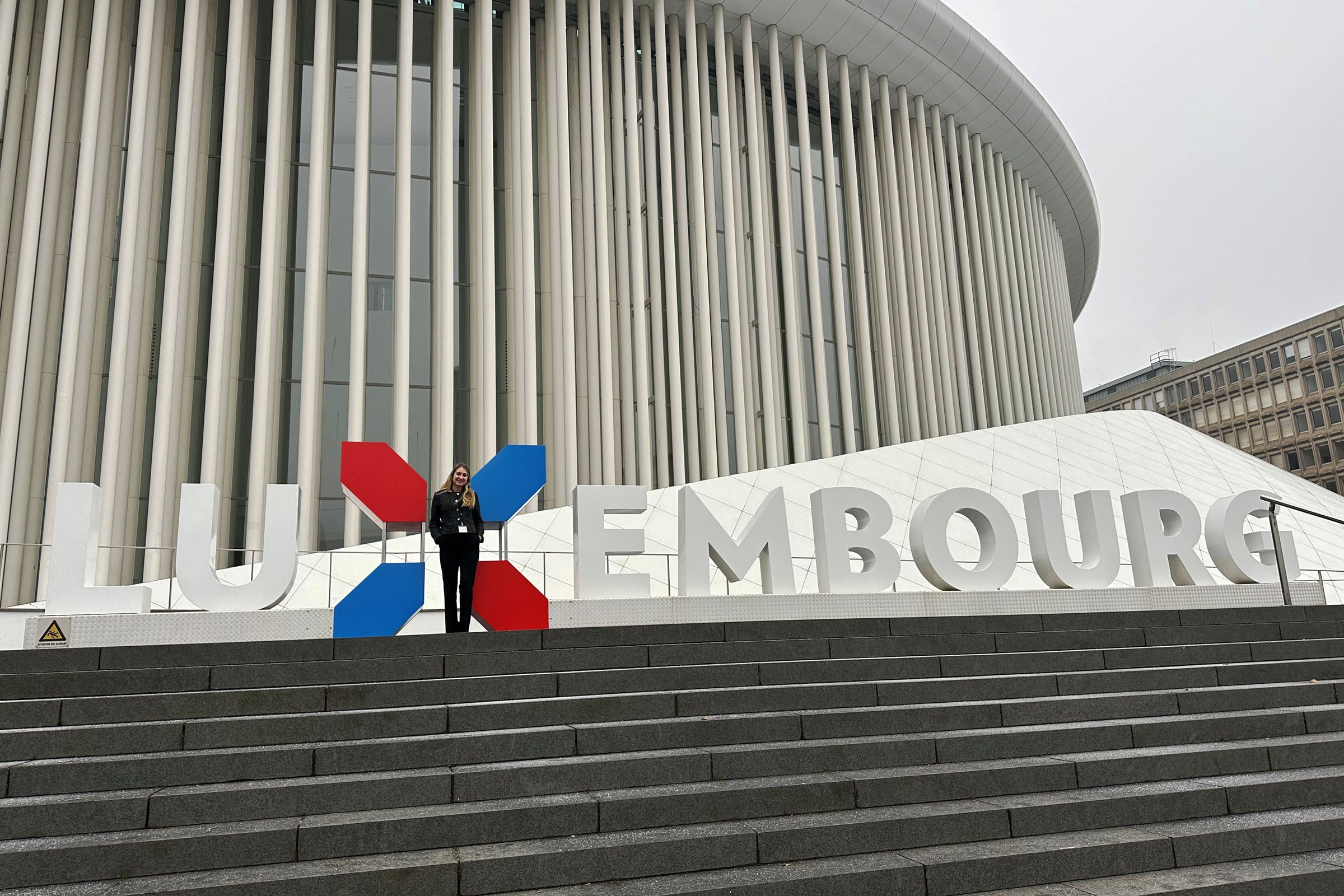 Emily Kohn stands in front of a large sign that spells out Luxembourg.