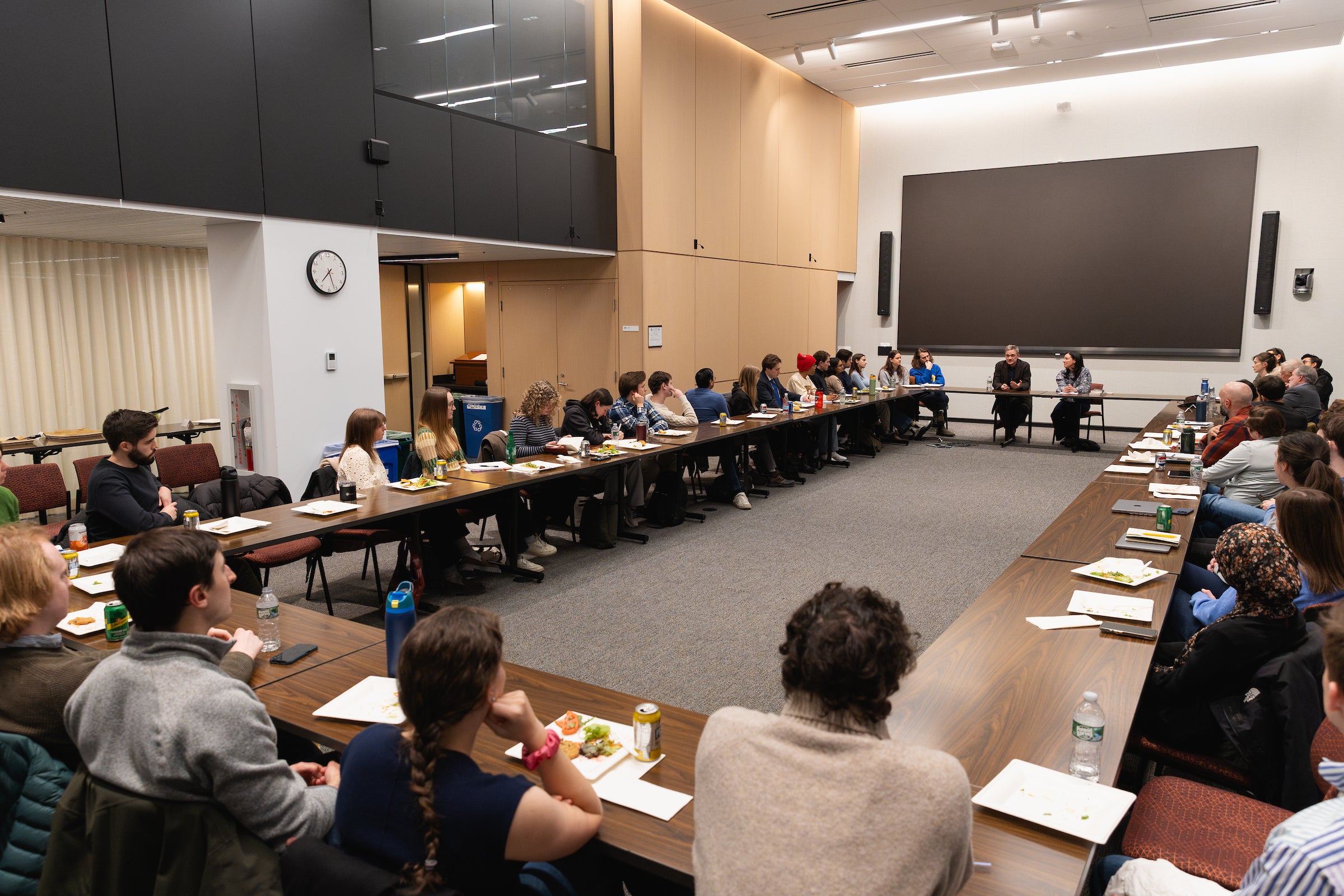 Patrick Radden Keefe speaks to a room full of attendees seated around tables arranged in a large rectangle.