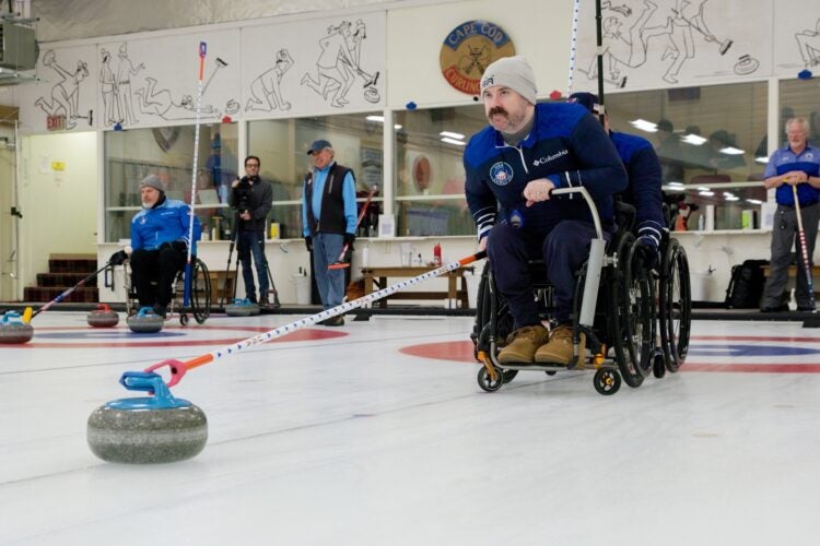 man in a wheelchair pushing a curling stone with a stick.