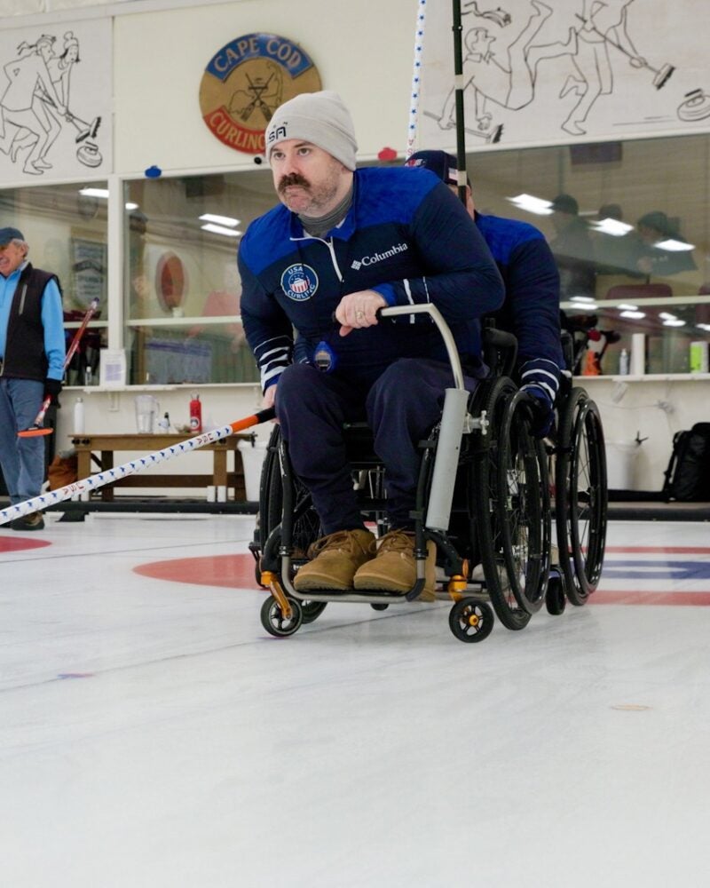 man in a wheelchair pushing a curling stone with a stick.