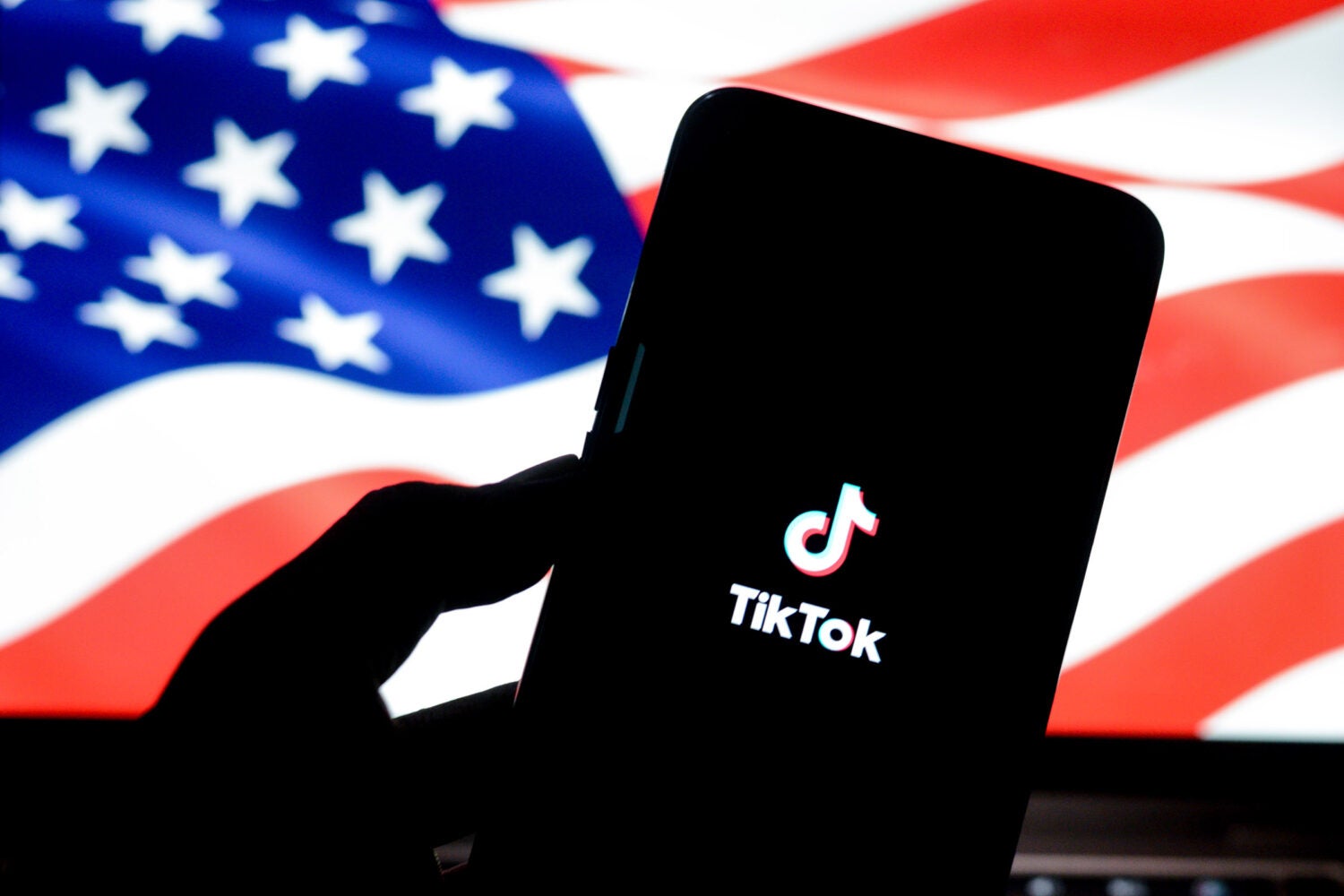 A phone displaying the TikTok logo with the American flag in the background.