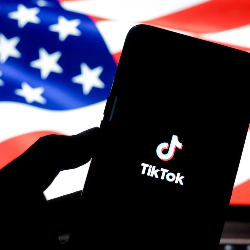A phone displaying the TikTok logo with the American flag in the background.