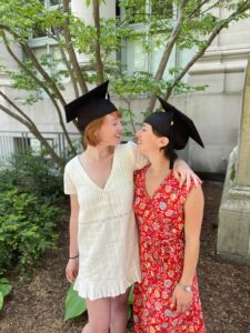 Couple wearing graduation caps looks lovingly at each other.