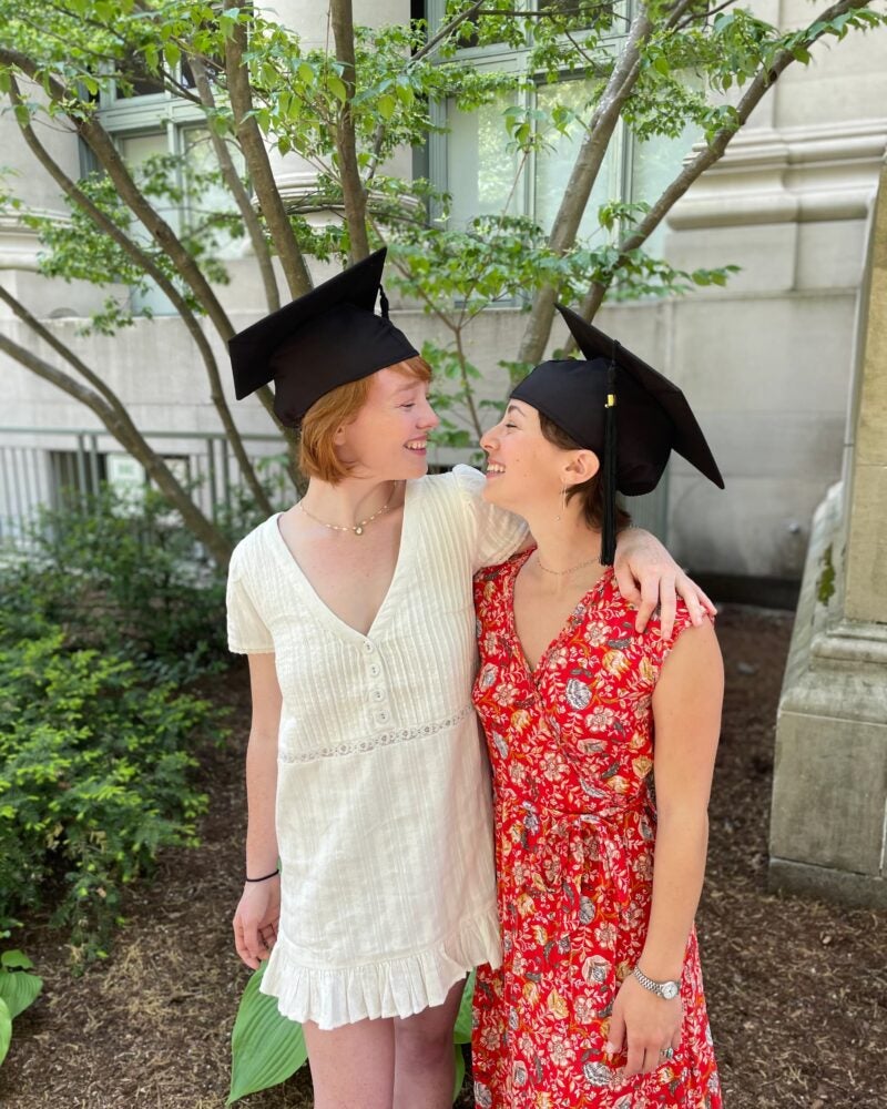 Couple wearing graduation caps looks lovingly at each other.
