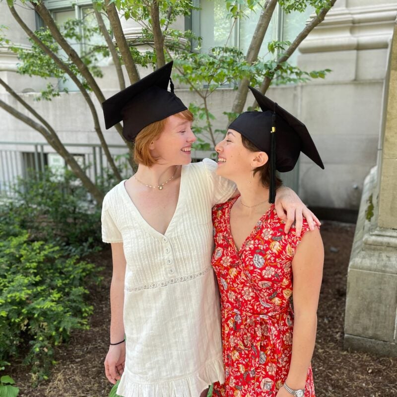 Couple wearing graduation caps looks lovingly at each other.