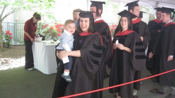Woman in regalia carries baby offstage after receiving diploma.