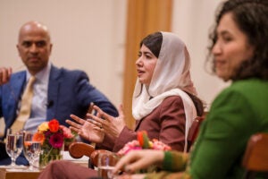 Malala Yousafzai speaking while Guhan Subramanian and Gaisu Yari listen.