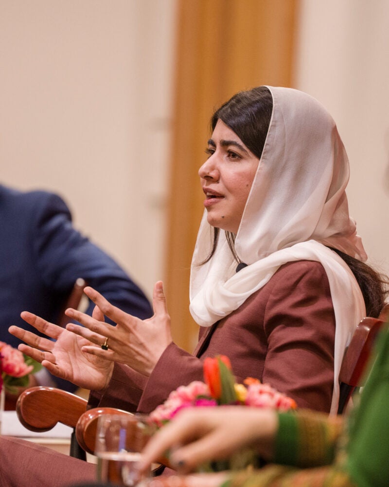 Malala Yousafzai speaking while Guhan Subramanian and Gaisu Yari listen.