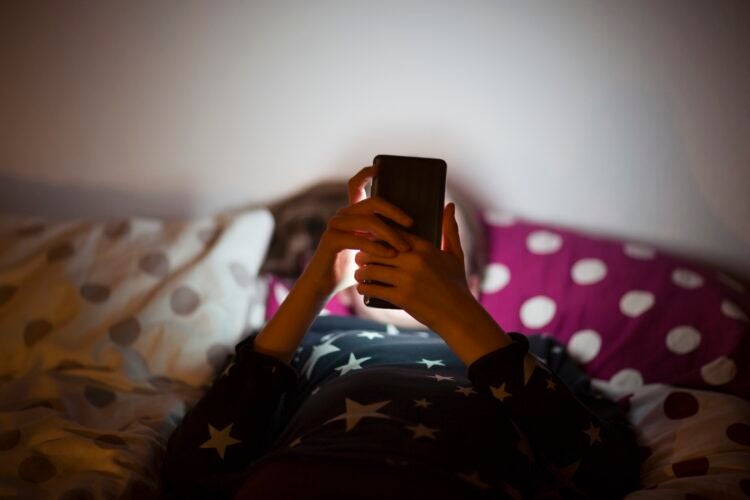 child in bed looking at the glow of a phone.