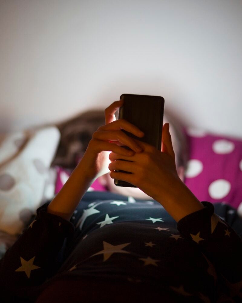 child in bed looking at the glow of a phone.