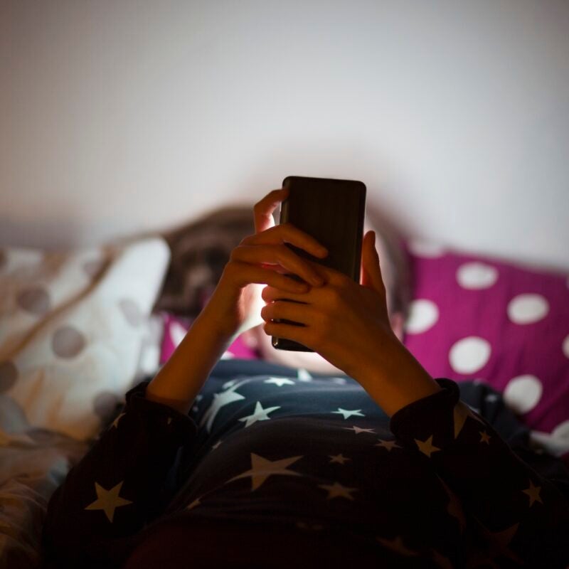 child in bed looking at the glow of a phone.