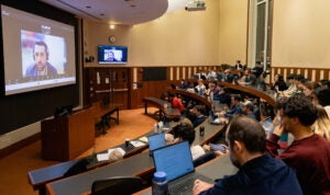 A view of a classroom with a speaker on the screen.