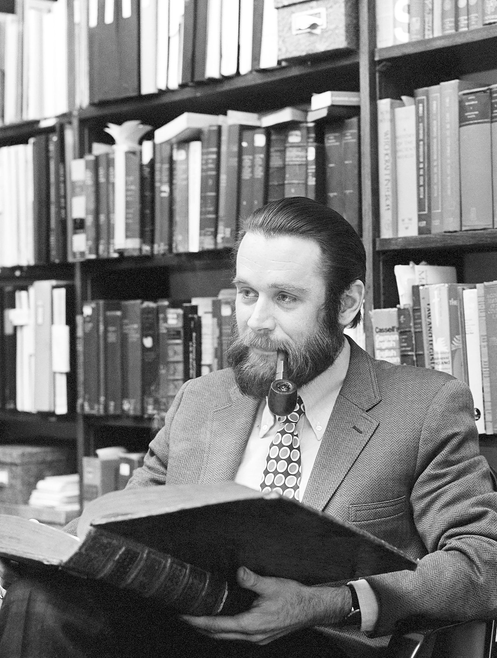 Charles Donahue pictured with a pipe in front of a bookshelf of old books.