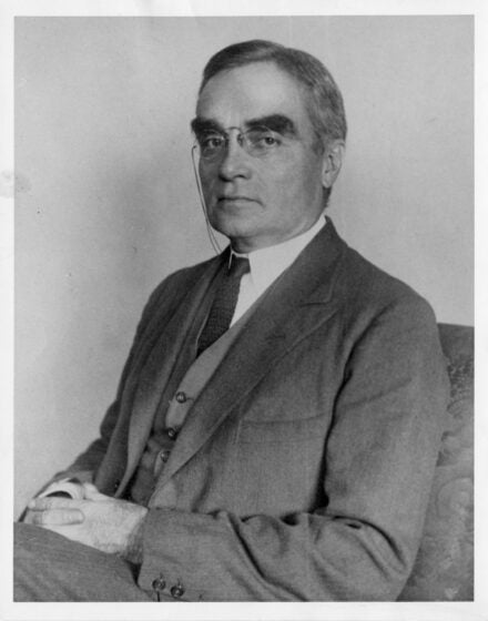 Portrait of Learned Hand sitting, hands folded in lap, wearing pince-nez glasses.