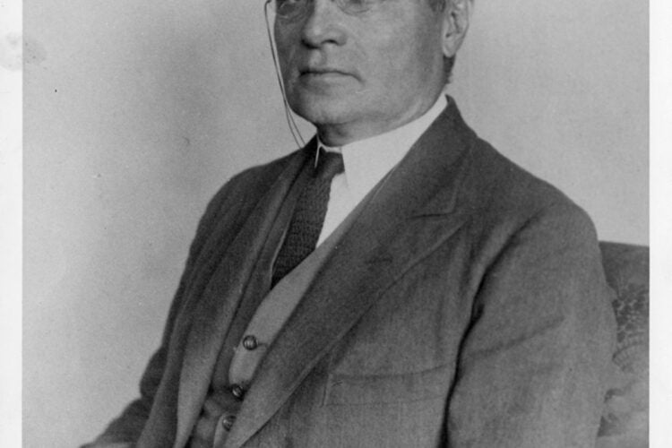 Portrait of Learned Hand sitting, hands folded in lap, wearing pince-nez glasses.