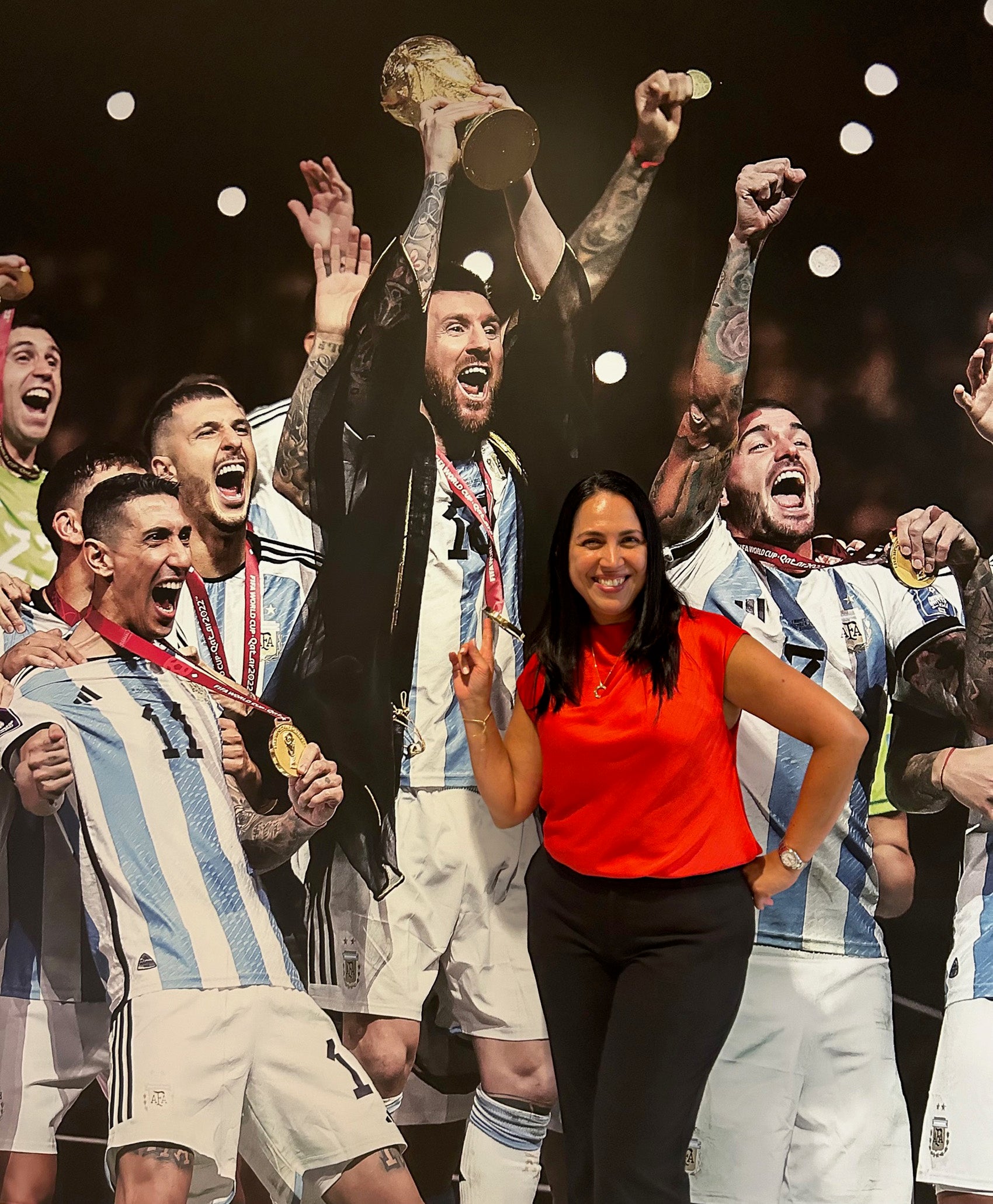 A woman poses in front a poster of cheering soccer players.
