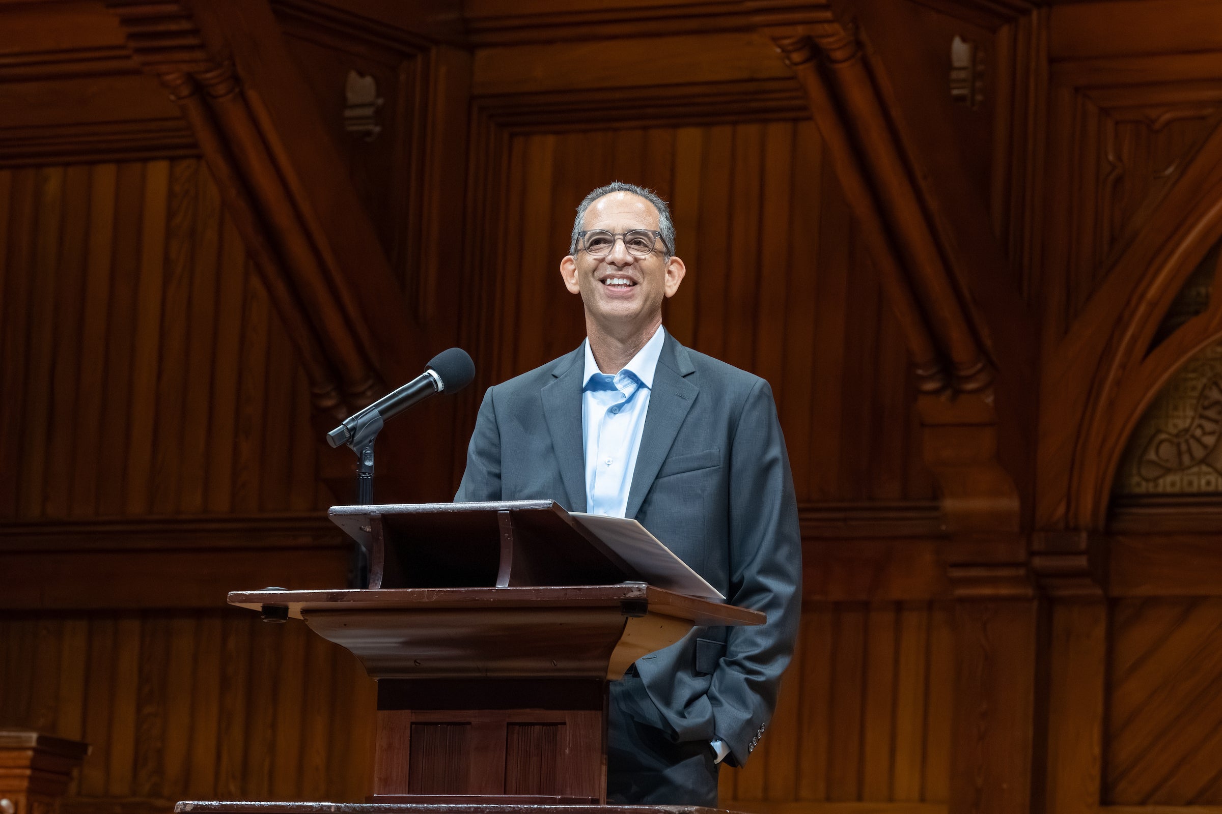 Dean Goldberg, standing behind a podium and microphone, smiles and looks out at the audience.