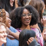 A closeup of several students in a larger group photo, smiling and talking with each other.