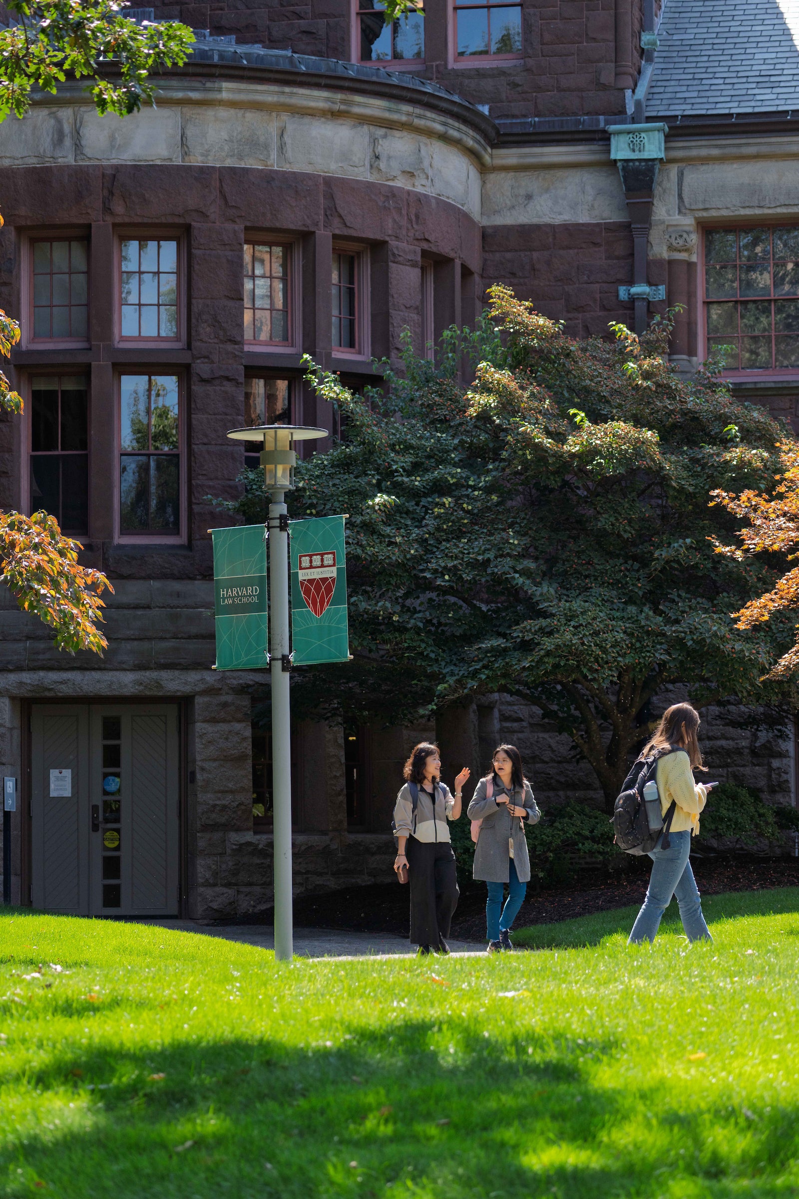 Students walk in front of a historic building made with red brick, with green grass in the foreground.