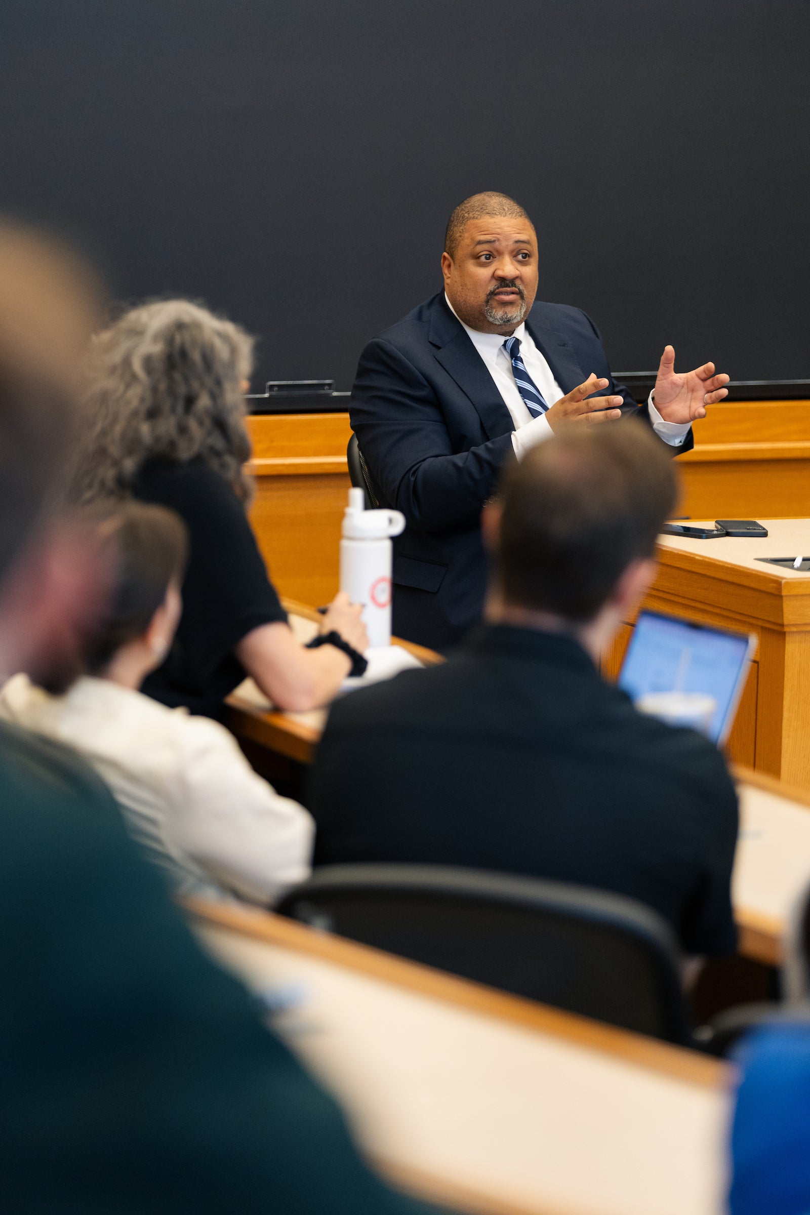 Alvin Bragg sits behind a desk and speaks to an audience in a classroom.