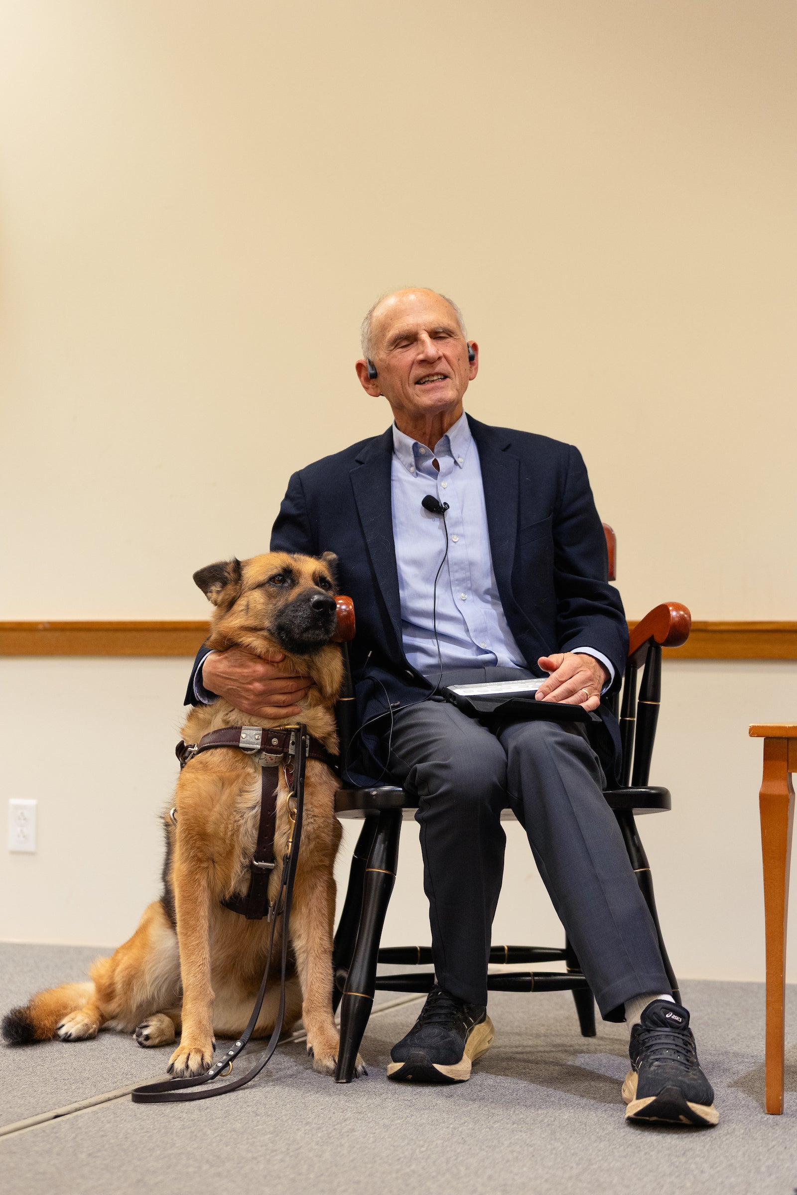 A man sits on a stage with an arm around his service dog.