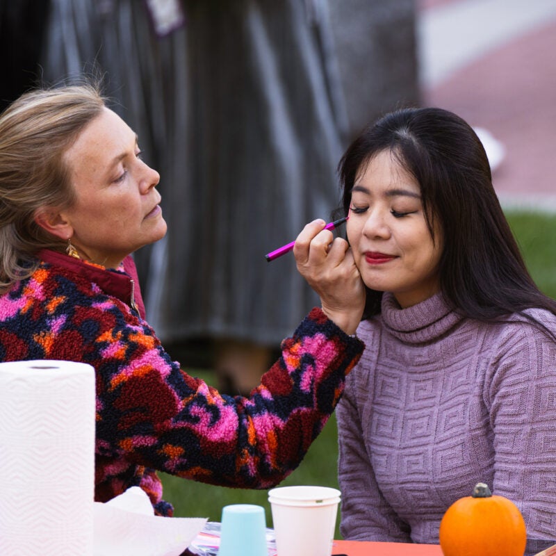 A woman paints a floral design on a student's face.