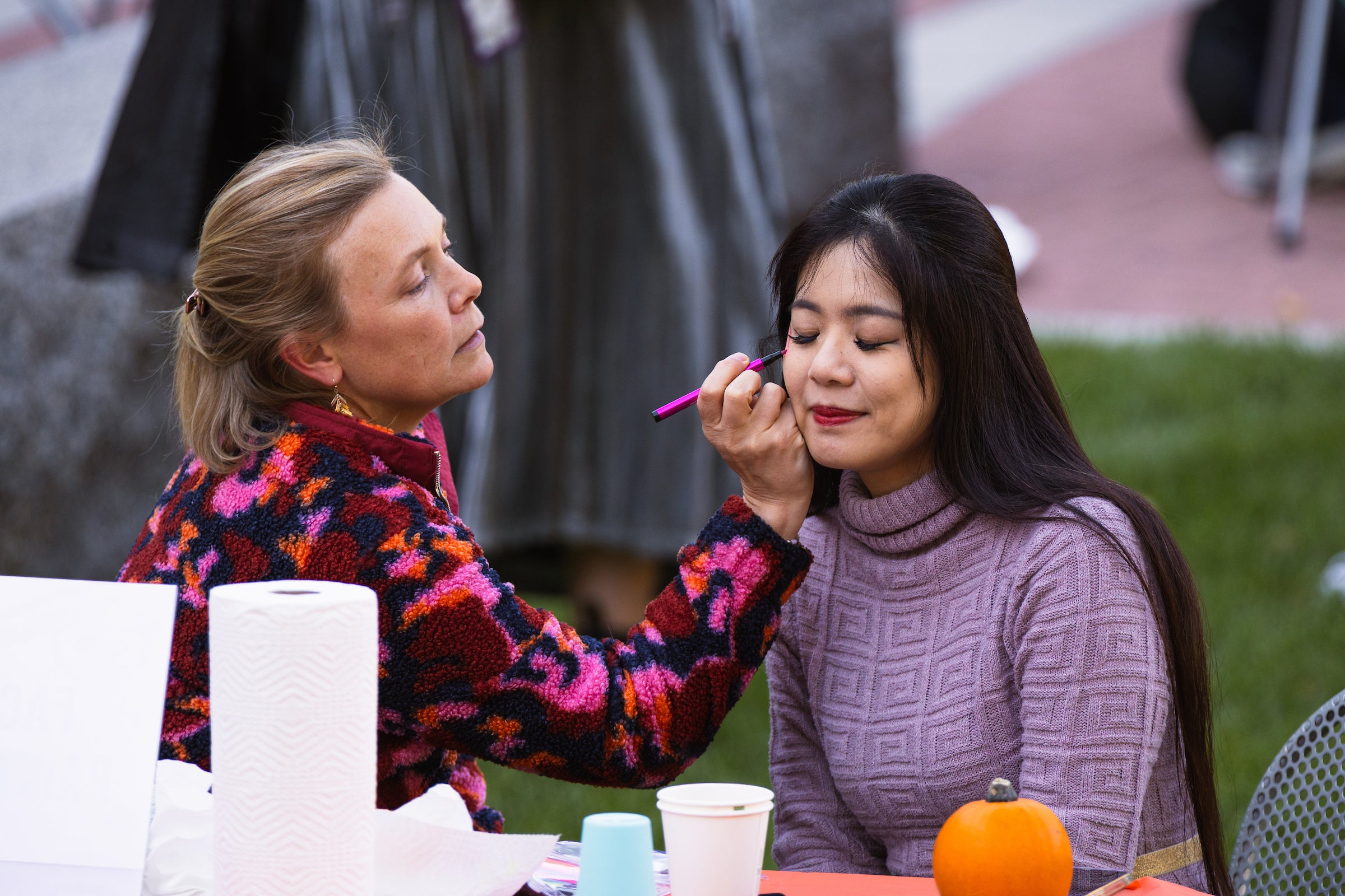 A woman paints a floral design on a student's face.