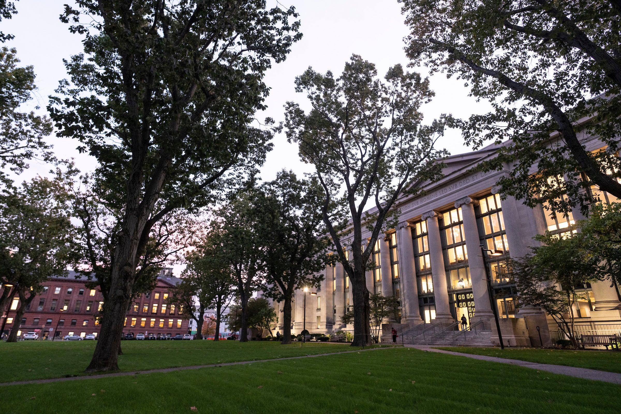 A building lit from within as it starts to get dark, surrounded by trees.