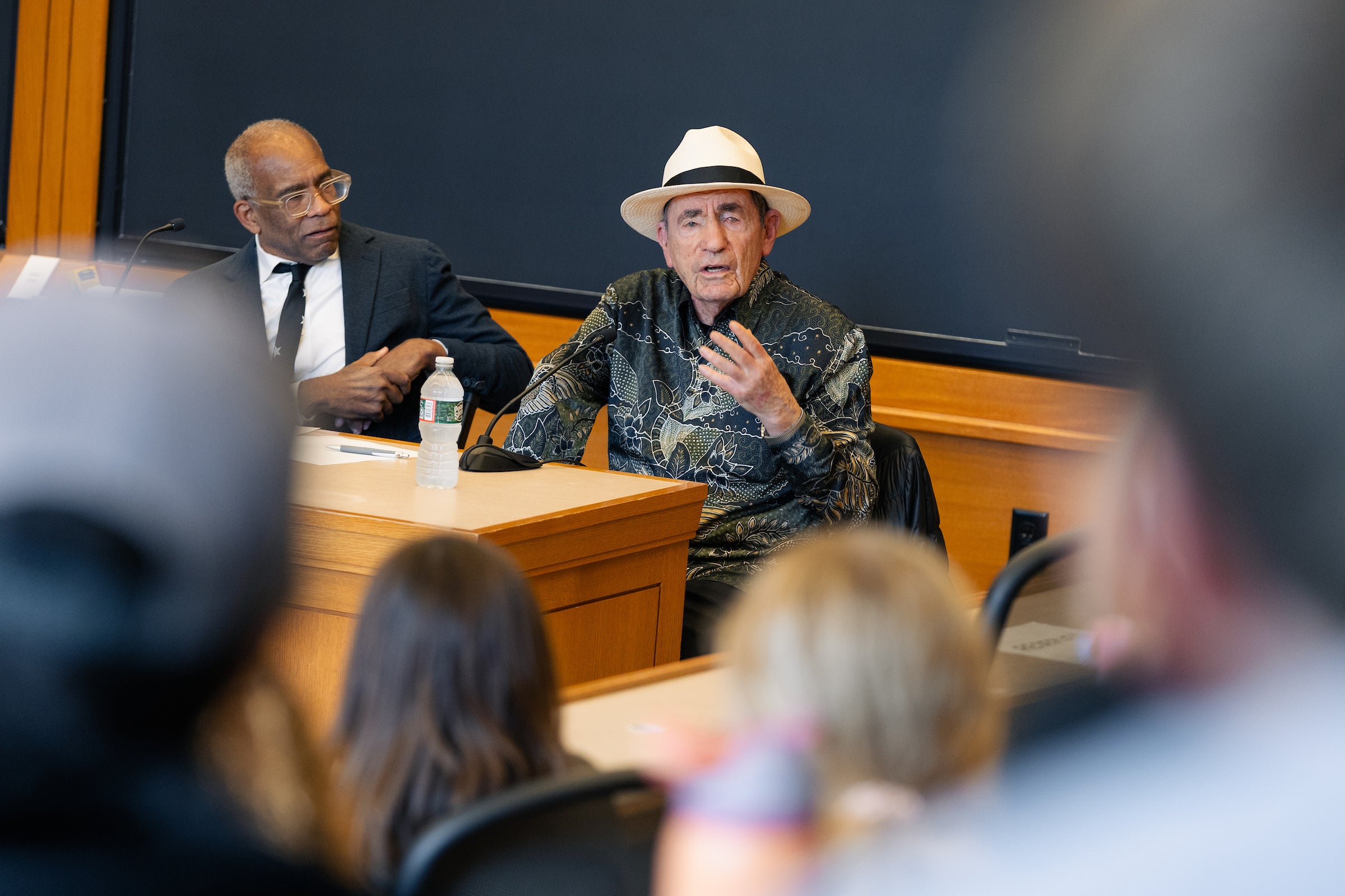 Albie Sachs, seated next to Professor Randall Kennedy, speaks to the audience in a classroom.