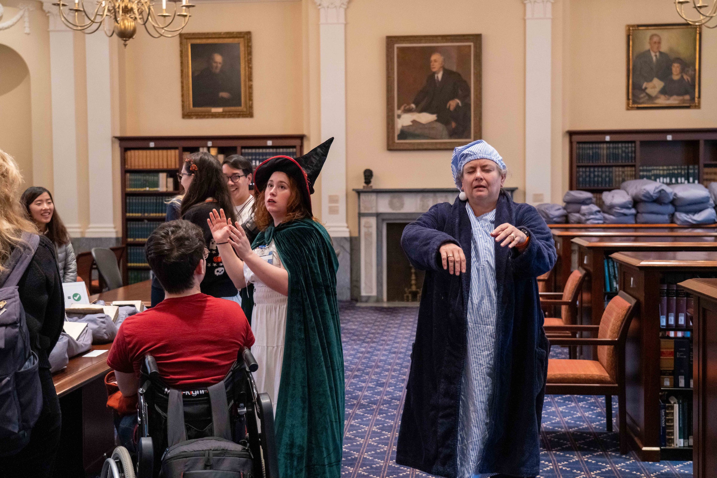 Two people in costumes, one in a witch hat and one in old-fashioned bedclothes, give a performance at a tour in a library.