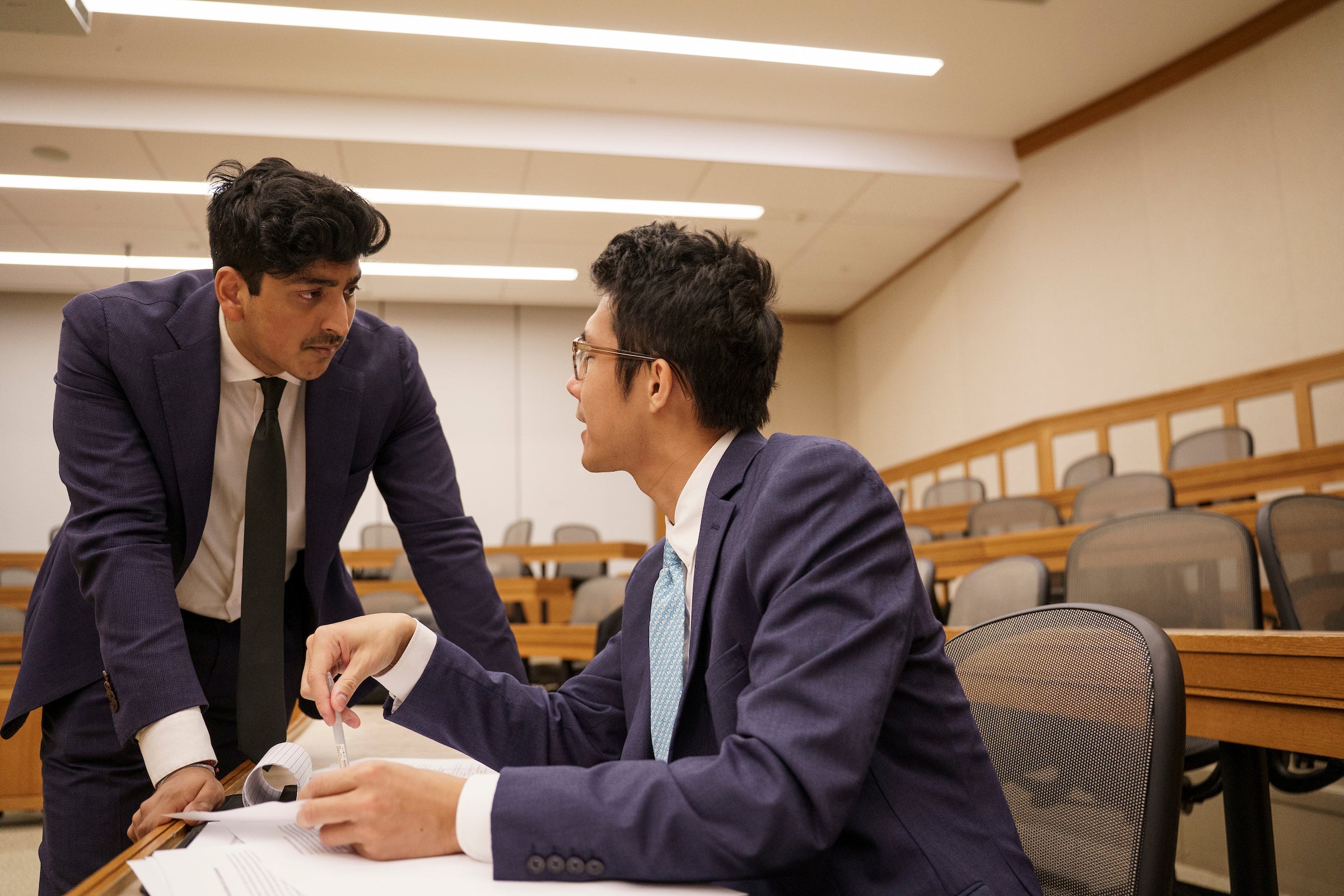 Two students speaking to each other ias they review papers in a classroom