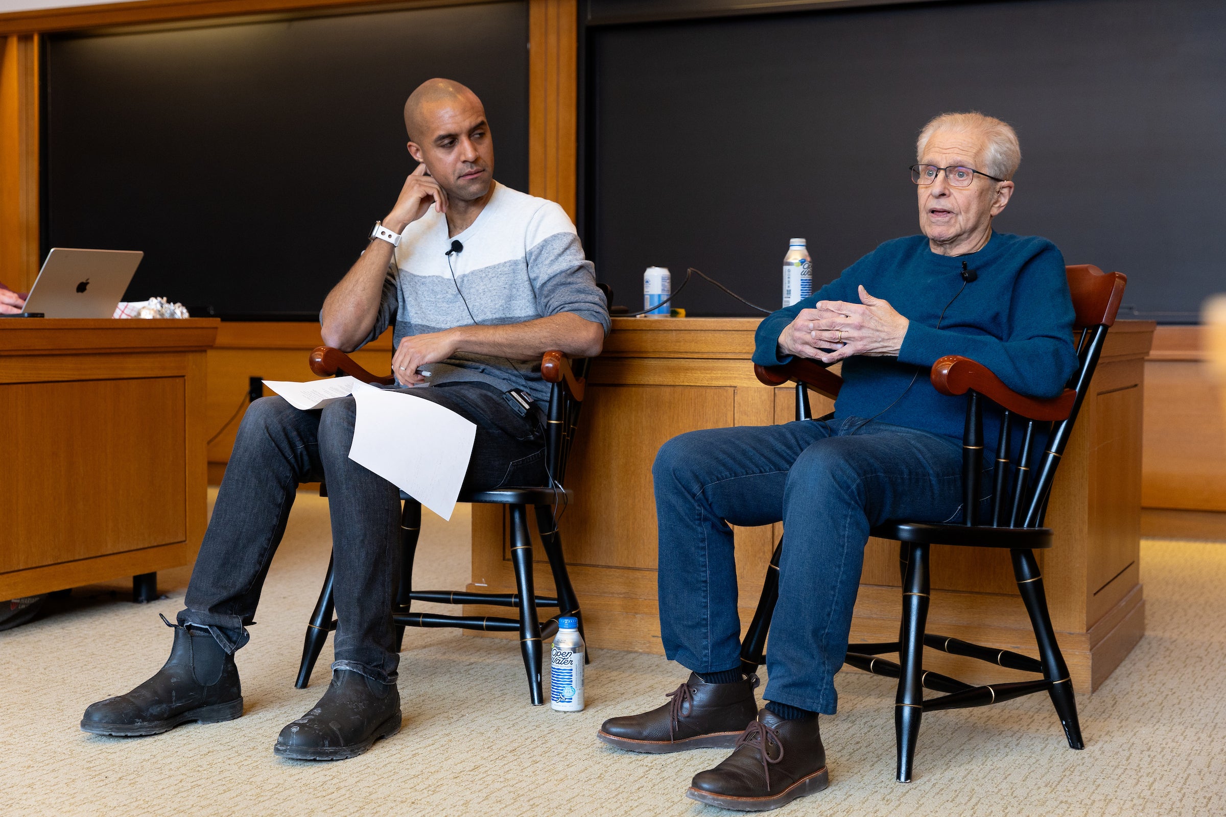 Two professors sit in chairs in a classroom.