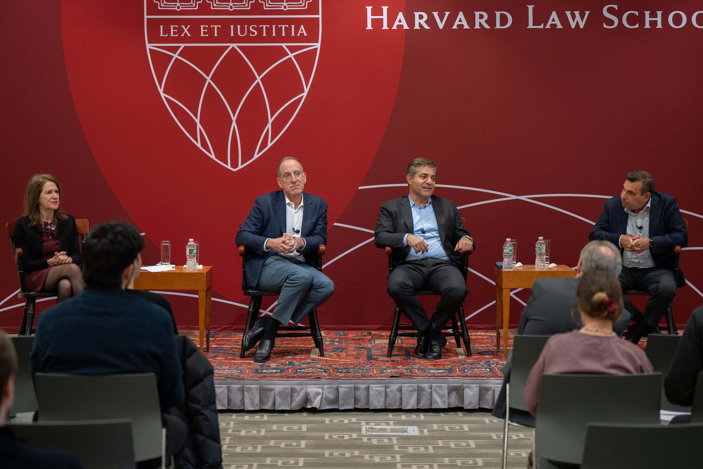 Four people sit on a stage and speak to an audience.