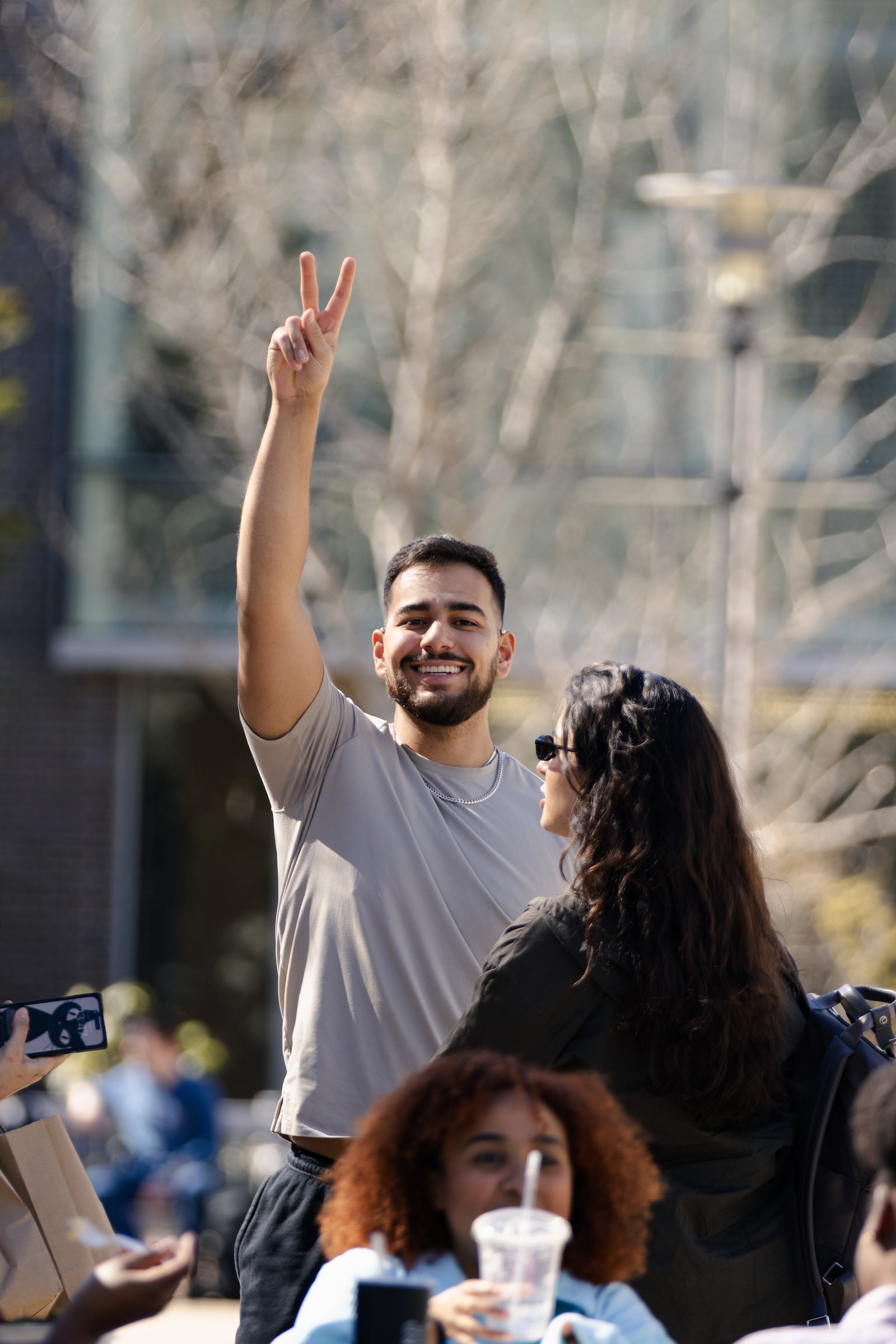 A student smiles and throws up a peace sign to the camera on a sunny day.