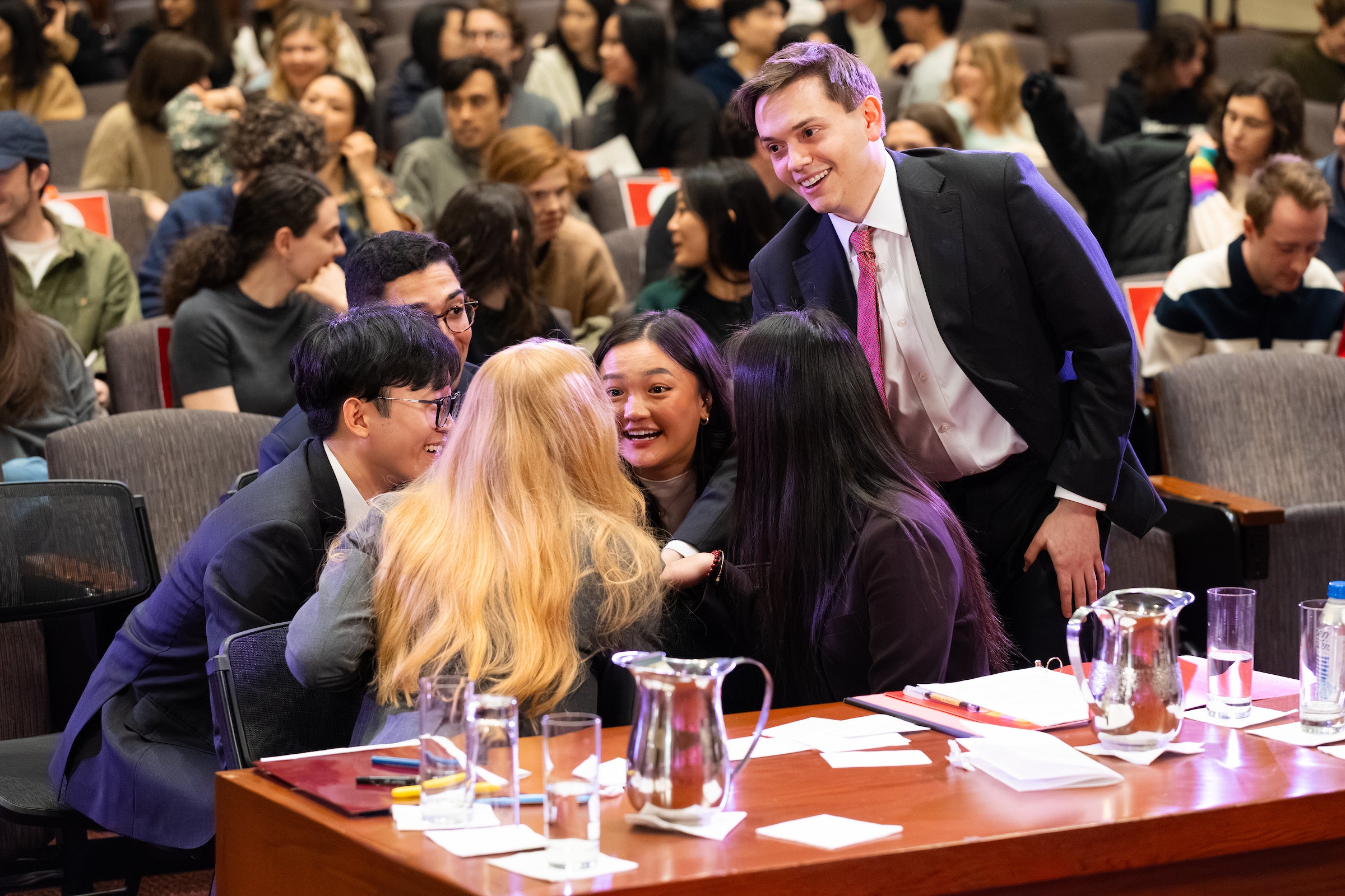 A team of students sitting behind a desk congratulate each other.