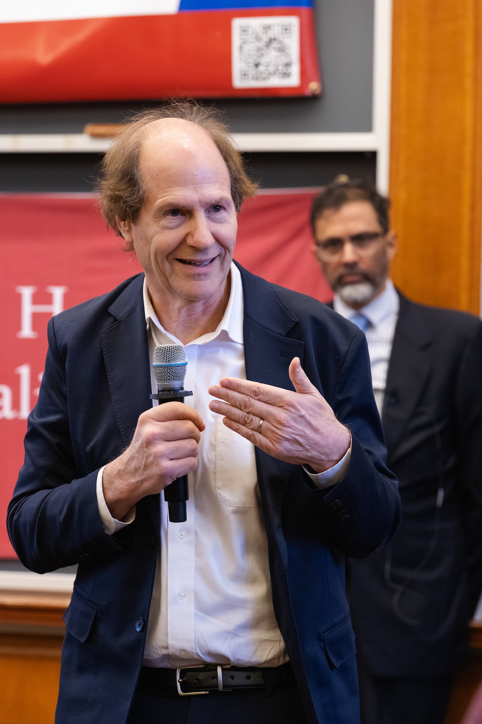 Professor Sunstein speaks into a microphone while Saikrishna Prakash stands behind him.