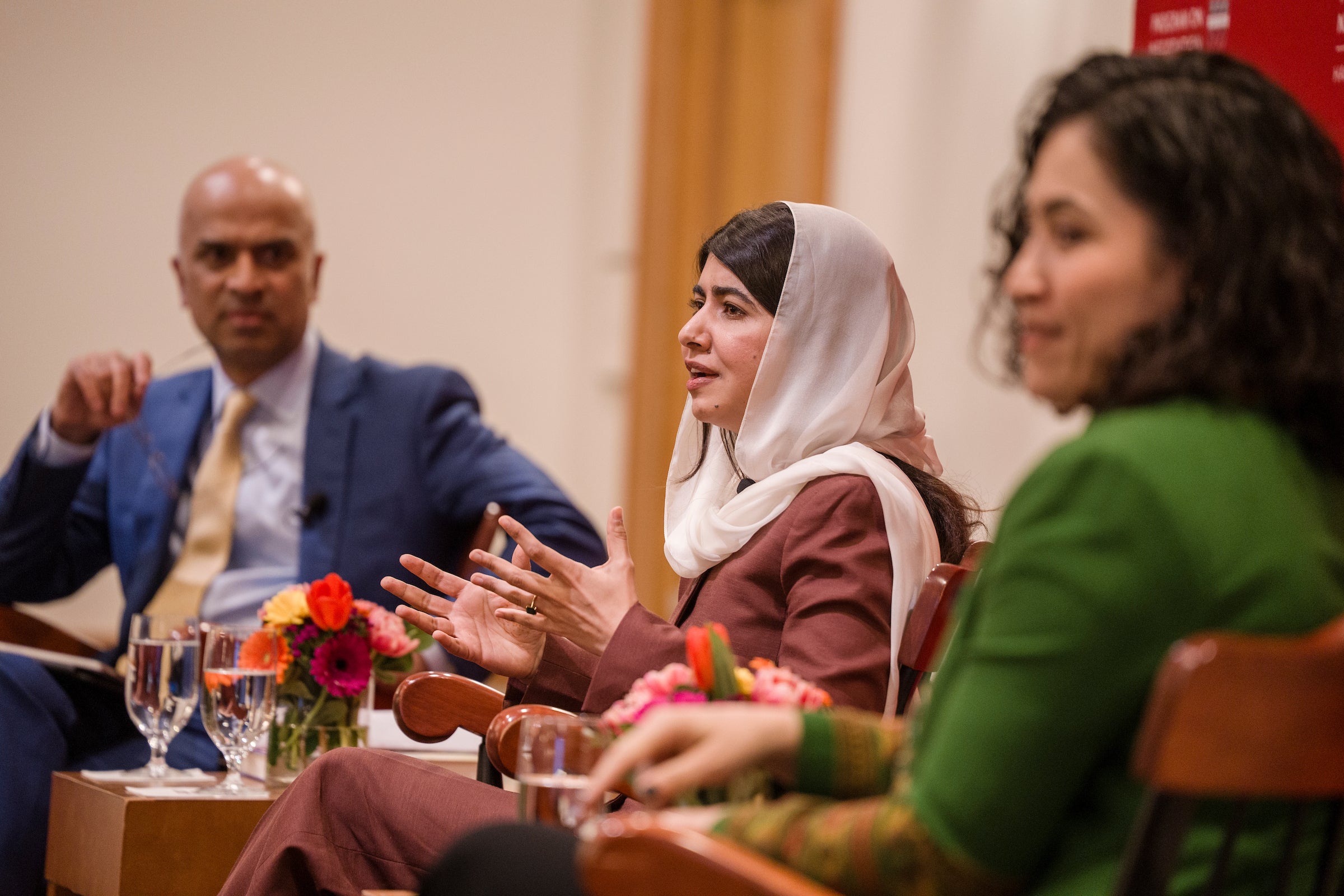 Malala Yousafzai sits on a stage with Gaisu Yari and Guhan Subramanian and speaks to an audience.