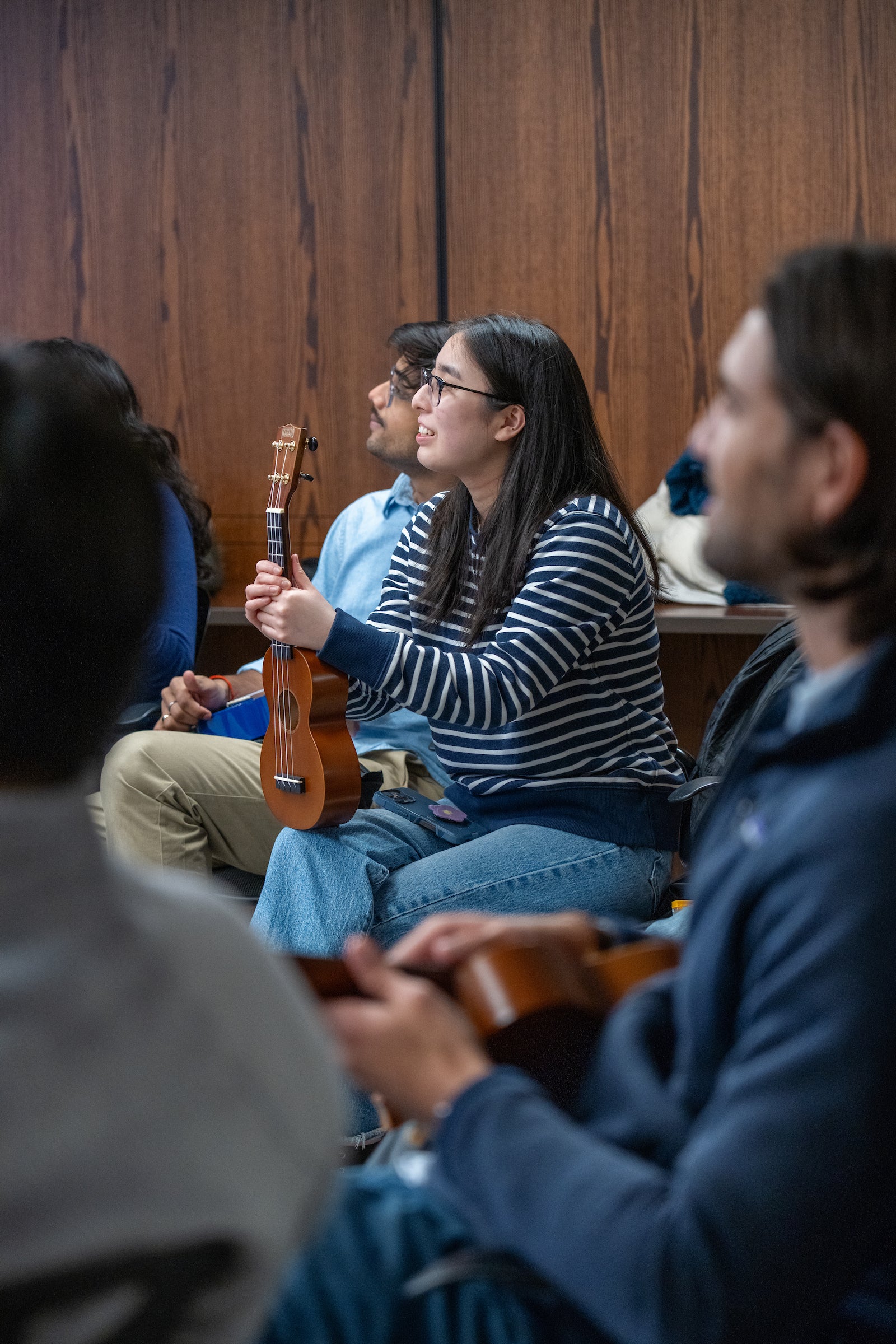 Students hold ukuleles and listen to instruction.