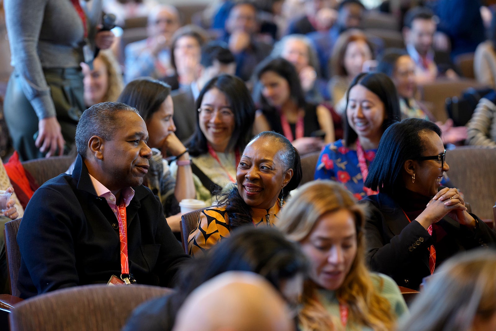 People sit in an audience, laughing and talking to each other.