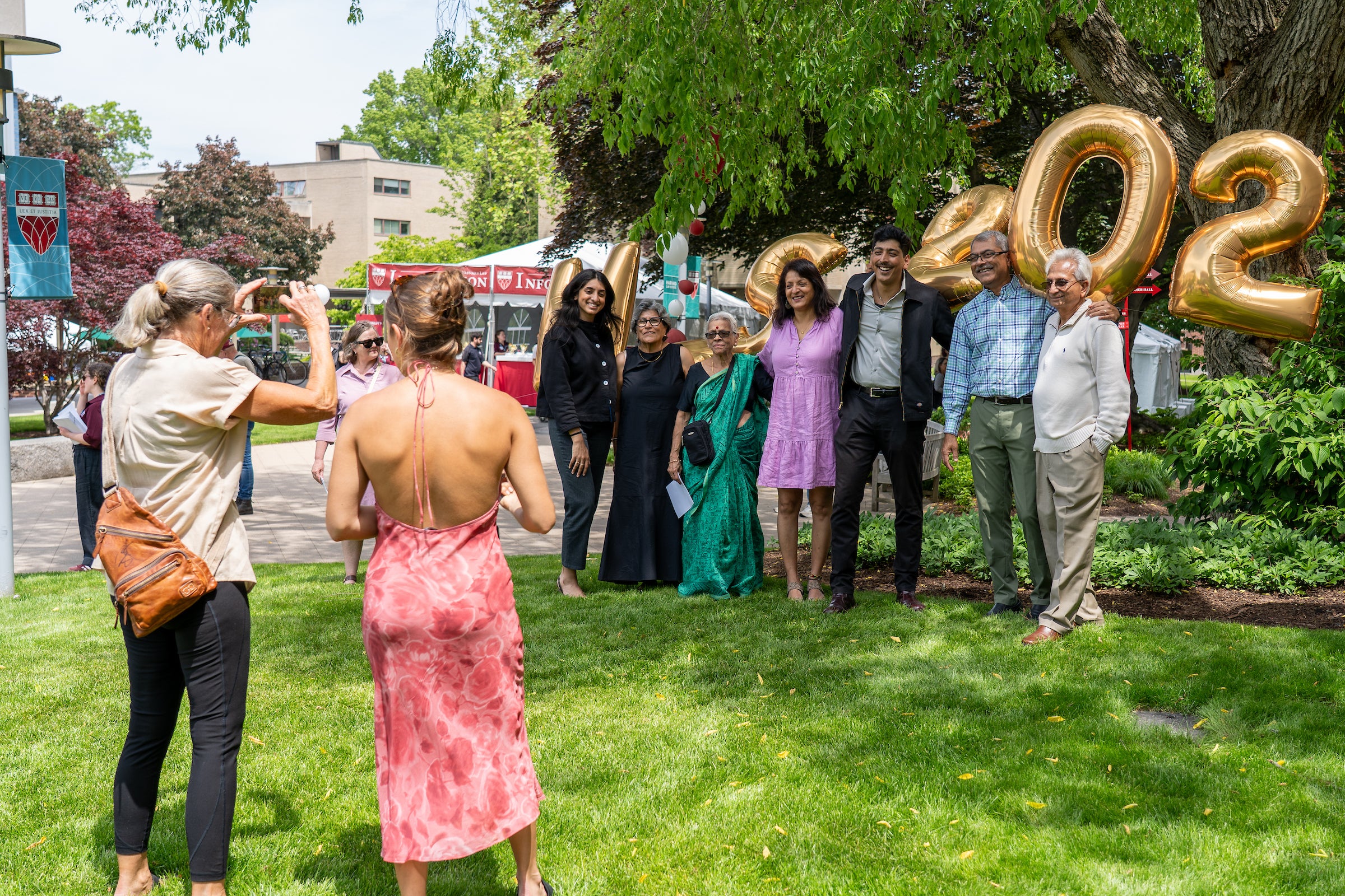 A group of people pose for a photo outdoors in front of large gold balloons on a sunny day.