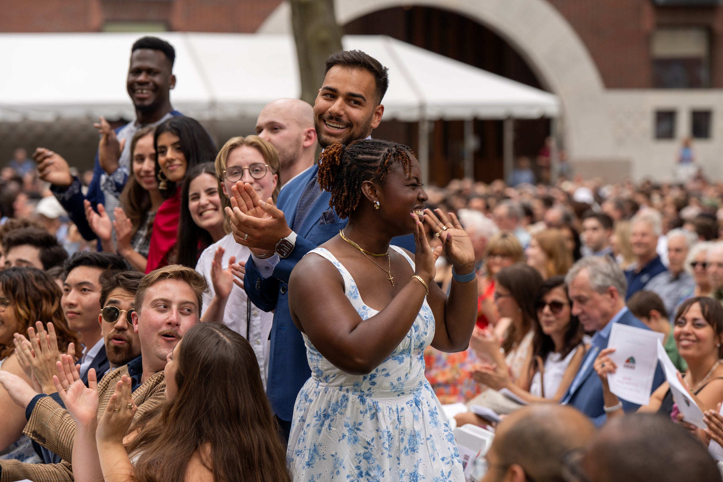 A person in a blue and white floral dress waves to an audience as she receives a round of applause.