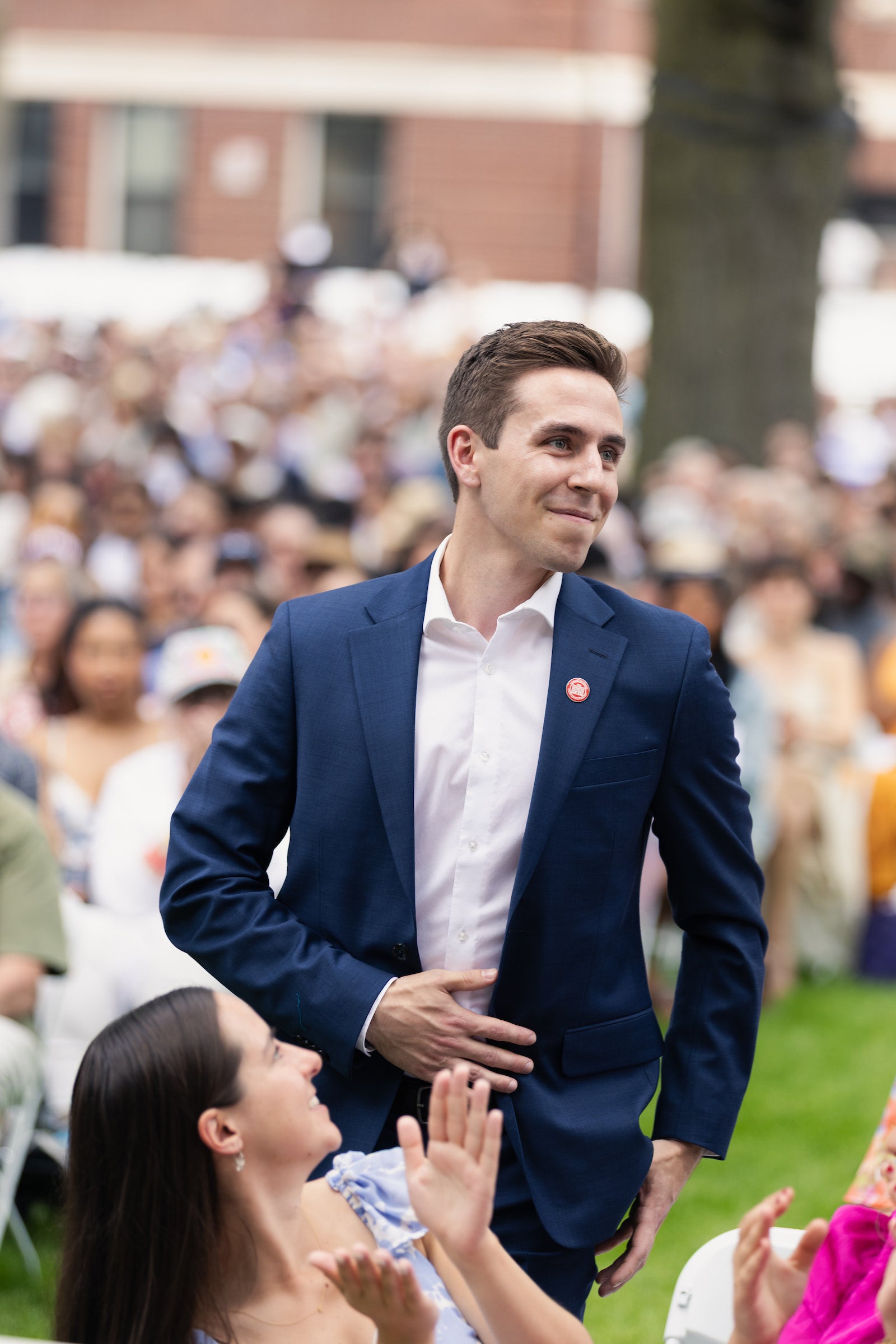 A person in a suit stands among an audience, smiling as they receive applause.
