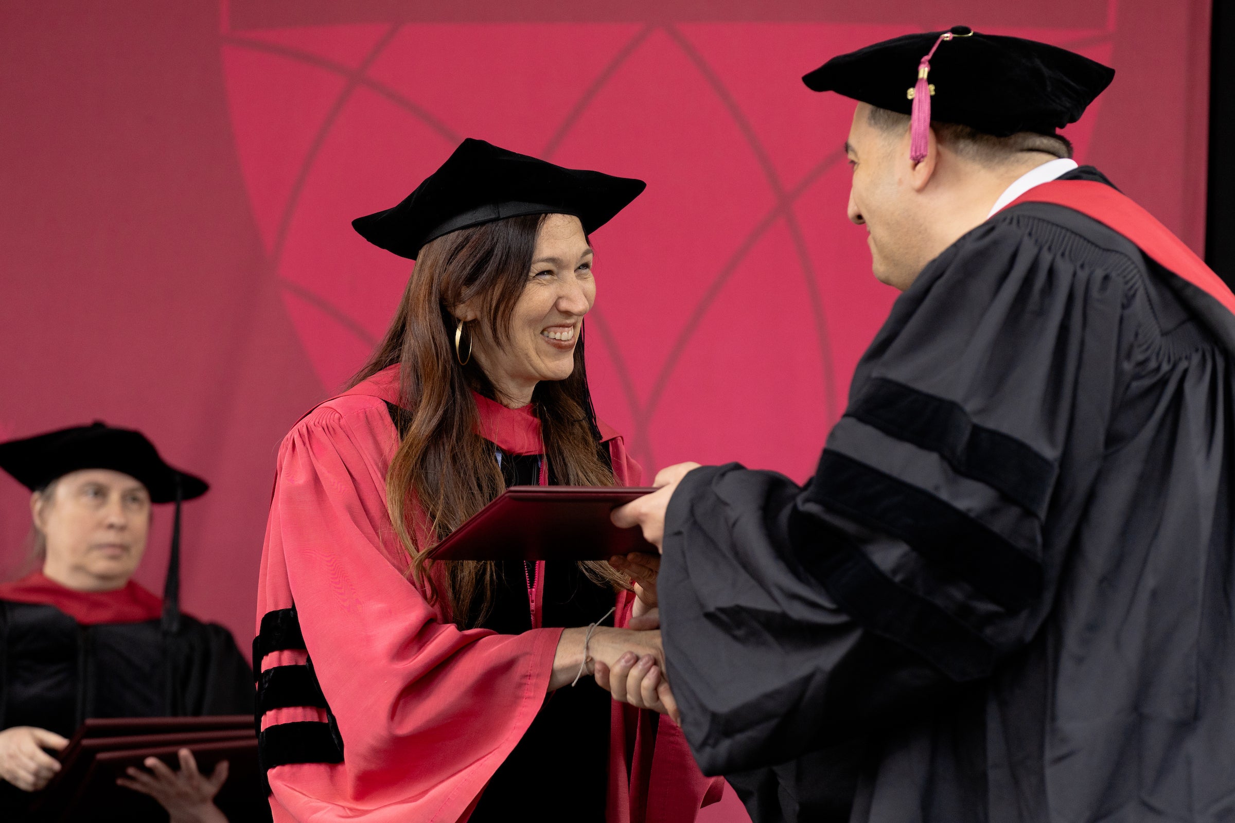 A Harvard Law professor shakes a graduate's hand as they accept their diploma.