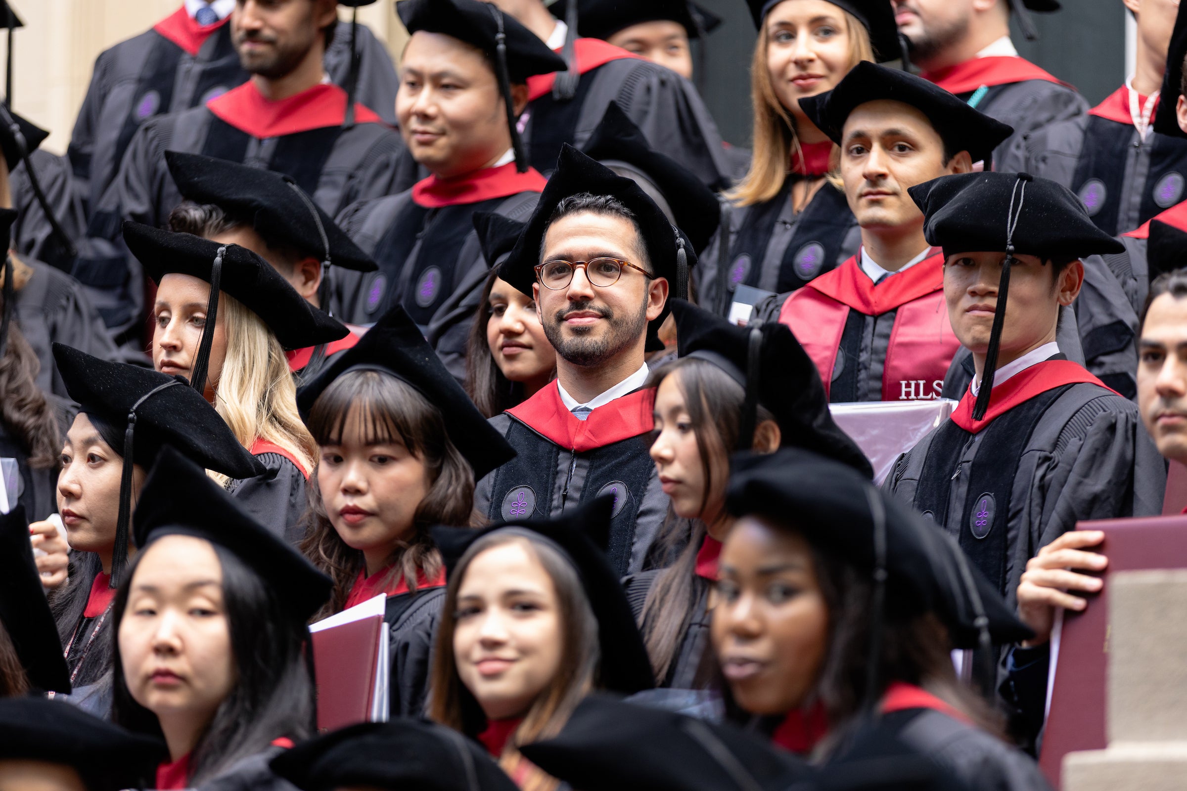A group of graduates in black caps and gowns with red accents stand together before posing for a photo.