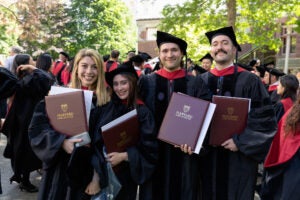 Four graduates in academic regalia smile for a photo with their diplomas.