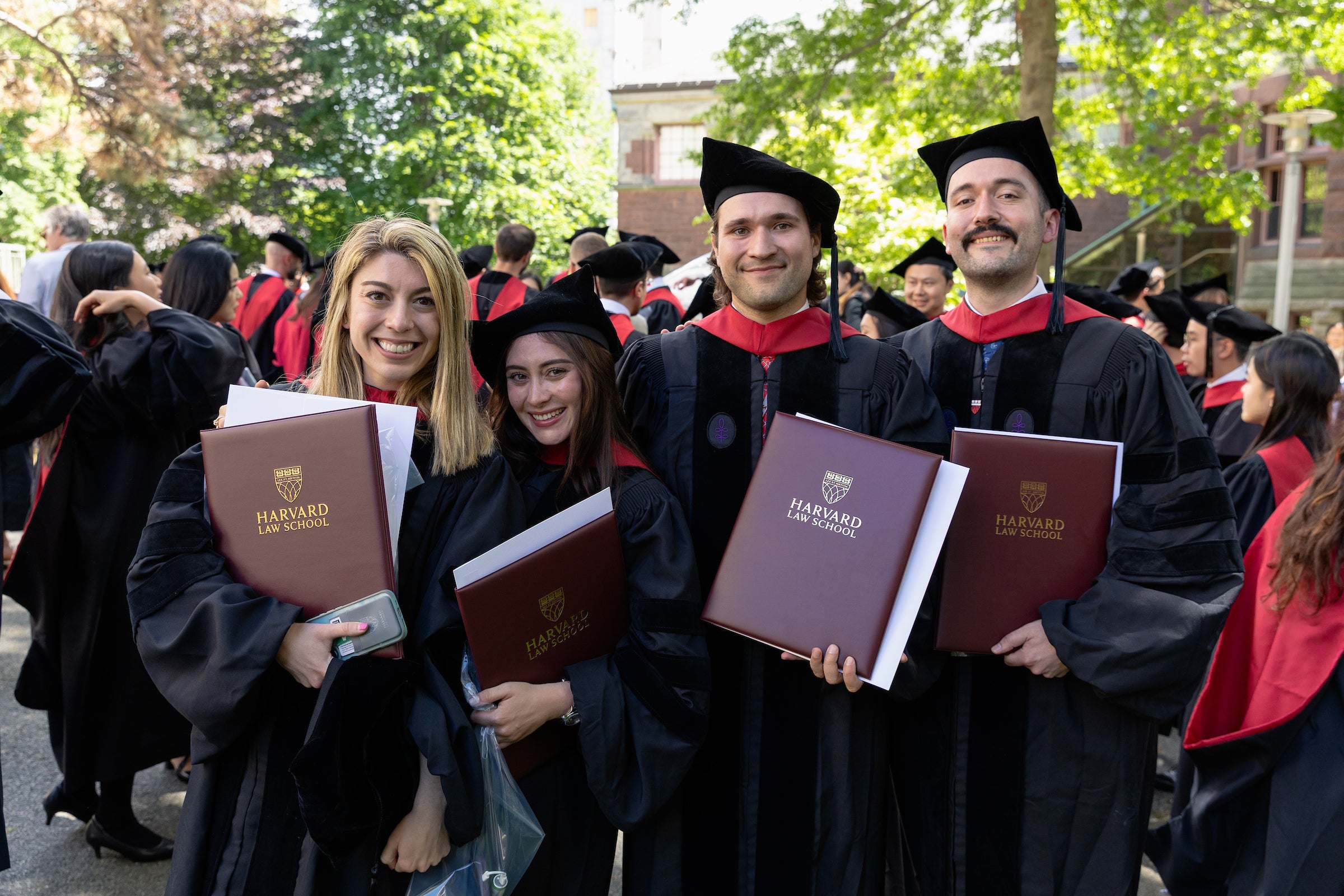 Four graduates in academic regalia smile for a photo with their diplomas.