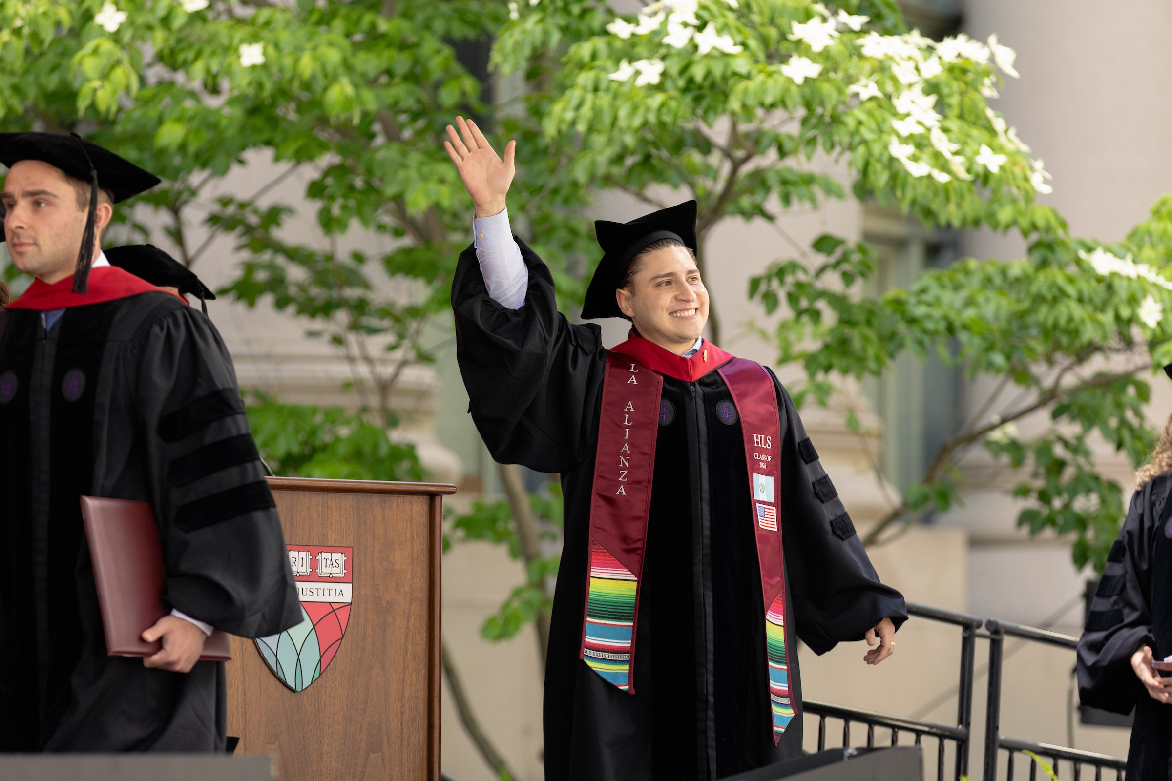 A graduate in academic regalia waves to the crowd before they cross the stage to accept their diploma.